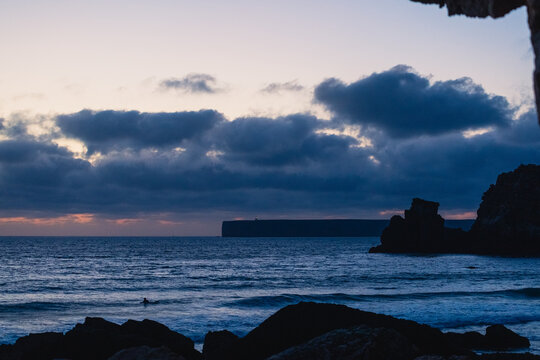 Surfer riding waves at sunset in sagres, algarve, portugal