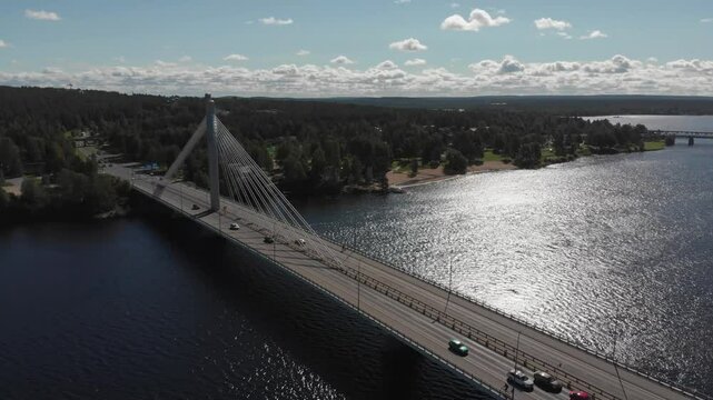 Slow aerial view of Rovaniemi, Kemijoki and  the J&auml;tk&auml;nkynttil&auml; bridge in Finland, drone flies over the river in summer with sun