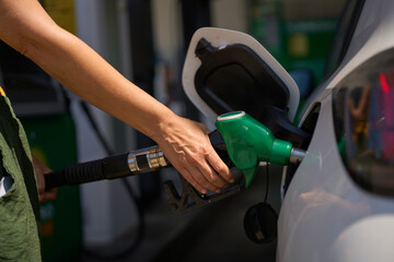 Woman refueling car at gas station, holding green fuel pump nozzle - fuel and oil price raise crisis