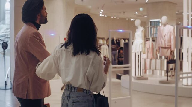A man and woman enter a clothing retail store, continuing their mall shopping experience.