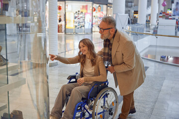 Family moment at shopping mall, mature granddad helping his granddaughter in a wheelchair