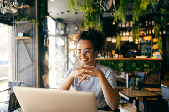 Cheerful remote worker sitting in cafe and smiling at the laptop.
