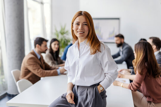 Portrait of businesswoman sitting on table and smiling at camera during seminar.