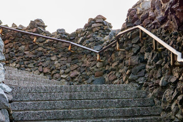 Stone stairs surrounded by a wall made of irregular rocks, with metal handrails on both sides.