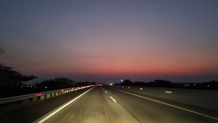 Empty highway road at sunset with light trails. Modern asphalt road at night with glowing markings. A highway disappearing into the distance with dramatic night sky in a rural landscape. Car advertisi
