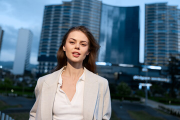 Confident business woman in a stylish blazer standing outdoors, featuring a modern city skyline in the background and showcasing professionalism and elegance.