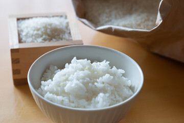 テーブルの上の茶碗に盛ったご飯、枡に入った白米と米袋
