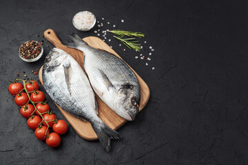 Fresh raw dorado fish with tomatoes spices and salt on dark background