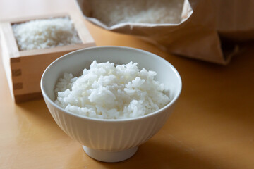 テーブルの上の茶碗に盛ったご飯、枡に入った白米と米袋