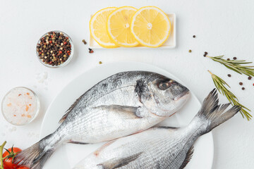 Close up of two dorado fish on white plate with lemon and tomato