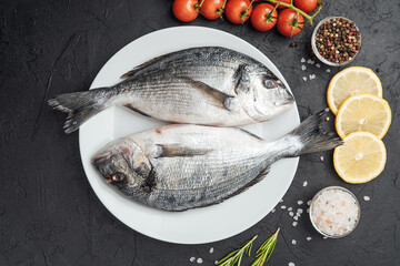 Fresh raw dorado fish on white plate with lemon tomatoes and spices