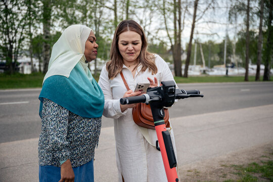 Two women using smartphone to rent electric scooter outdoors