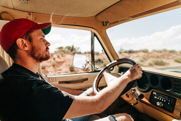 Man in red cap driving vintage vehicle through desert landscape
