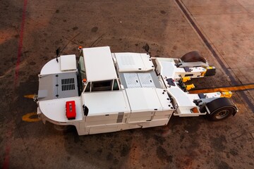 A high-angle view shows a white aircraft towing tractor on the airport apron, crucial for maneuvering aircraft. Essential ground support equipment ready for operation in the aviation industry.