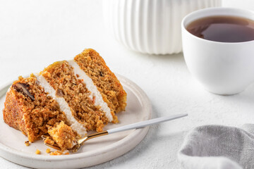 Homemade layered carrot cake with cream cheese, walnuts and spices on a plate with tea