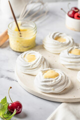 Meringues mini pavlova cakes with lemon cream served on a tray on white marble background. Light summer dessert