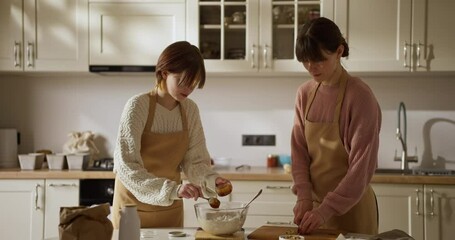 Girl amateur baker adding honey to dough while baking and teamwork with her mom in kitchen during family baking activity at home - Powered by Adobe