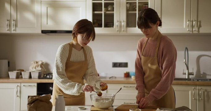 Girl amateur baker adding honey to dough while baking and teamwork with her mom in kitchen during family baking activity at home