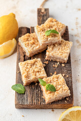 Lemon crumble bars on wooden cutting board on white tile background. Oatmeal lemon bars