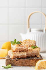 Lemon crumble bars on wooden cutting board on white tile background with text space. Oatmeal lemon bars