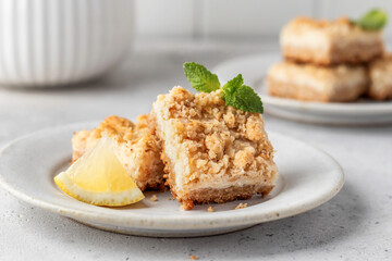 Lemon crumble bars served on a plate decorated with mint leaves on light gray background. Oatmeal lemon bars