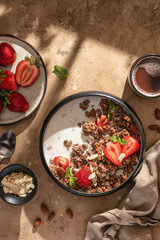 Healthy breakfast: fresh granola, muesli with milk, strawberry and almond for breakfast on brown textured background in bright morning light. Top view