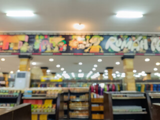 Blurred image of a supermarket or retail store interior with shelves full of various products. The out-of-focus scene creates an abstract effect of a brightly lit commercial space