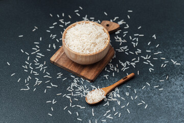 White rice in wooden bowl with scattered grains and wooden spoon