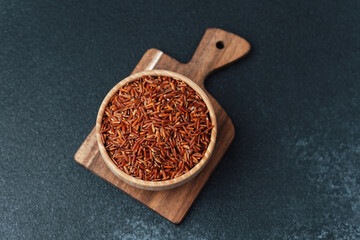 Red rice in wooden bowl placed on cutting board over dark surface