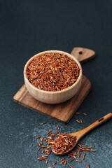 Red rice in wooden bowl on cutting board with scattered grains and spoon
