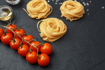 Tagliatelle pasta nests with tomatoes, oil, pepper and salt on black textured background
