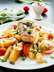 Plate with baked potatoes, piece of fish, vegetables and herbs on the table with tomato sauce. Dinner served with fish and chips meal.