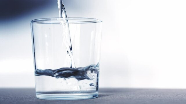 A transparent glass slowly fills with water . The glass is empty. The glass is sitting on a clean table. The image has a calm and peaceful mood