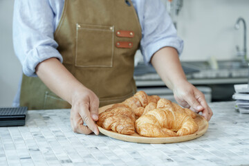 Close-up of Asian barista placing wooden plate of croissants on cafe counter, highlighting...