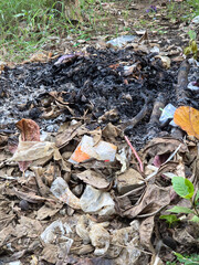 Close-up of outdoor burning pile with glowing embers and dry leaves in open field surrounded by...