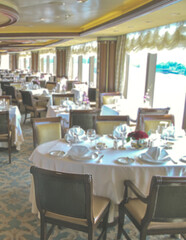 Formal and elegant ocean view dining room restaurant onboard luxury cruiseship or cruise ship liner with set tables in Art Deco interior design style and ceiling ambient lighting