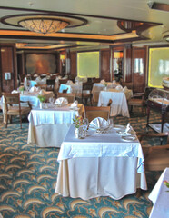 Formal and elegant ocean view dining room restaurant onboard luxury cruiseship or cruise ship liner with set tables in Art Deco interior design style and ceiling ambient lighting