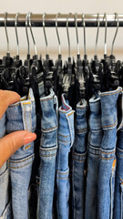 A woman's hand sorts through jeans hanging on hangers in a clothing store. Shopping process,...