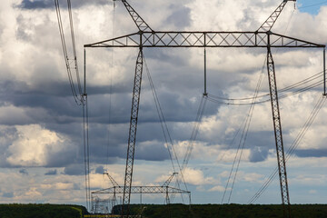 High-voltage power lines stretch across a scenic landscape with dramatic clouds in the sky during late afternoon light