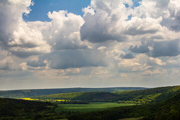 Scenic view of rolling hills and dramatic clouds over a lush green valley under a bright blue sky during midday