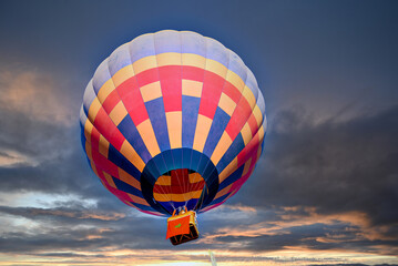 Colorful hot air balloon flying under orange sunset sky