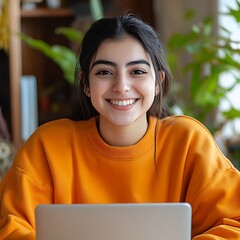 a young woman from Egypt working with laptop smiling in a bright orange sweatshirt
