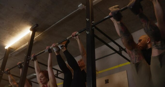 Group of athletic people doing Hanging Leg Raises to Bar during fitness class in modern cozy gym on horizontal bars. Review of sports people in sports and crossfit