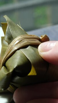 Hand holding zongzi rice dumpling with savoury fillings wrapped in bamboo or reed leaves.