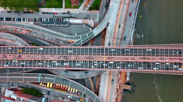 Traffic jams on the Brooklyn Bridge. Lots of people walk by the bridge. Cars move quickly by the roads and freeway below the bridge. New York, USA. Top view.
