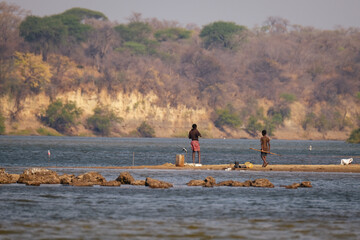 Fishermen stand on a sandbank in the Kavango River, between Namibia and Angola, in the Caprivi Strip, surrounded by serene waters and distant forested cliffs