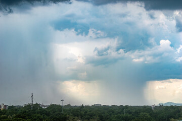 Dramatic cloud formations over a lush green landscape during an afternoon rainstorm in a city