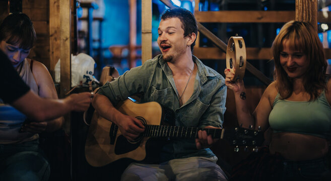 Friends gather in a warm ambiance as a guitarist and tambourine player create lively and joyful music, enhancing the cozy experience.