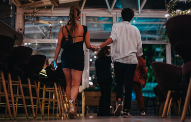 A fashionable couple walking hand in hand through a stylish, modern restaurant for a night out. They exude sophistication and excitement, perfect for nightlife or urban lifestyle themes.