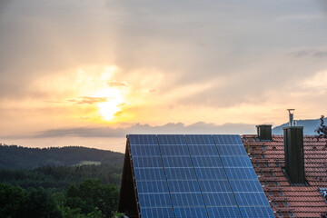 Solar panels on a house rooftop absorb evening sunlight to produce clean and sustainable green...